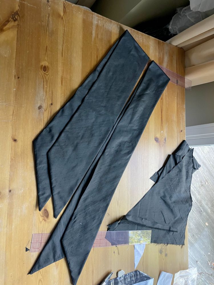 Two long black silk cravats folded in half on a wooden table