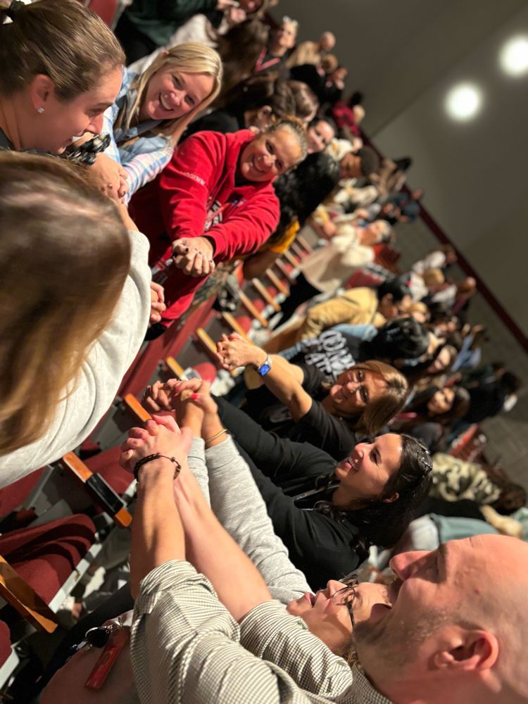 A group of workshop participants standing in a circle stretching their arms, smiling, and listening to someone talk