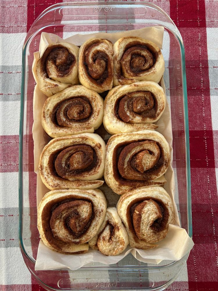 Cinnamon rolls in a glass baking dish that have risen overnight.