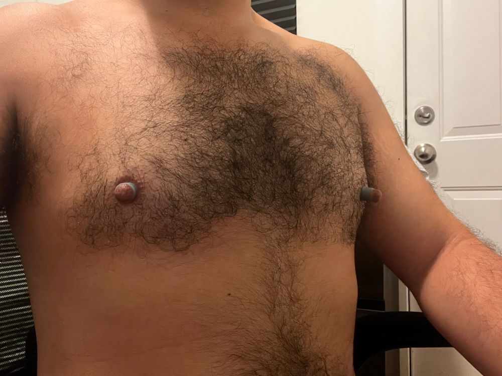 A hairy chested man wearing elastic bands around his pumped and enlarged nipples