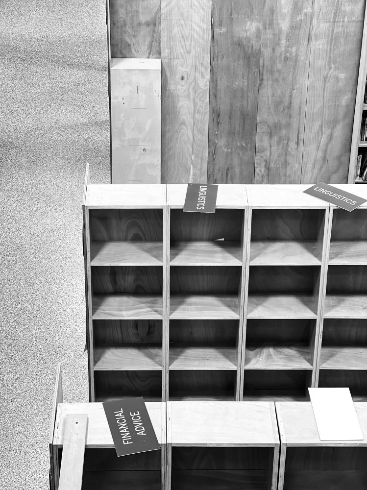 Empty bookshelves with signs placed on top. 