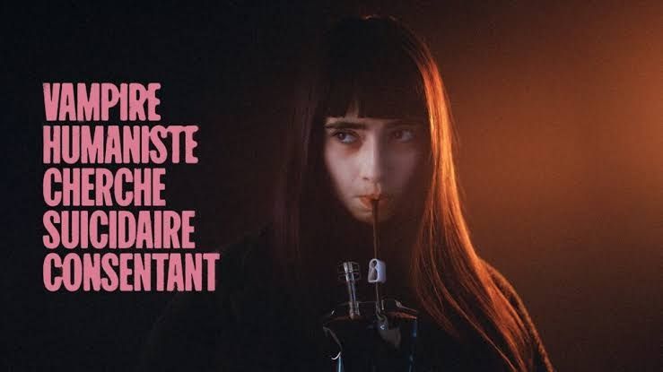 Pôster do filme “Vampira Humanista Busca Suicida Voluntário”
No meio da imagem, vê-se uma mulher jovem de cabelos escuros e lisos segurando uma bolsa de sangue com um canudo. O fundo é escuro do lado esquerdo e tem um brilho laranja à direita.