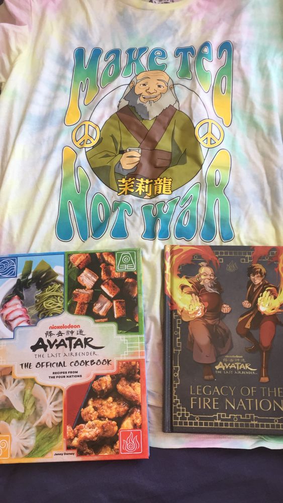 In this photo are two Avatar the Last Airbender books:
The Offical Cookbook
Legacy of the Fire Nation

The picture also contains a t-shirt with Uncle Iroh on it with “Make Tea Not War” as text surrounding him. The t-shirt is tie-dyed 