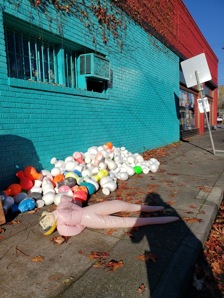 A very large pile of styrofoam heads (some even spray painted in neon colours!) and a blown out blowup doll outside of a well known Portland vintage resale shop. 