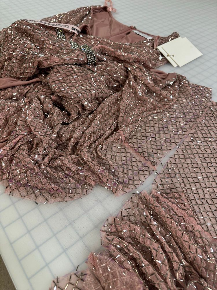A Mac Dougal beaded dress in a heap on the cutting table. It is a king of peachy taupe mesh with antiqued silver glass bugle beads. The bottom has just been cut off, and the cut edges are a few inches apart. The beads haven’t been removed from the bottom of the dress at this point. 