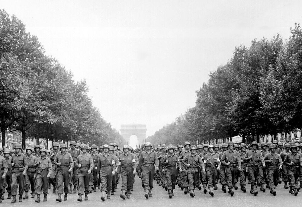 The black and white photo shows a large phalanx of white American soldiers marching down the Avenue des Champs-Élysées, in August 1944, during the military parade that marked the liberation of Paris. 