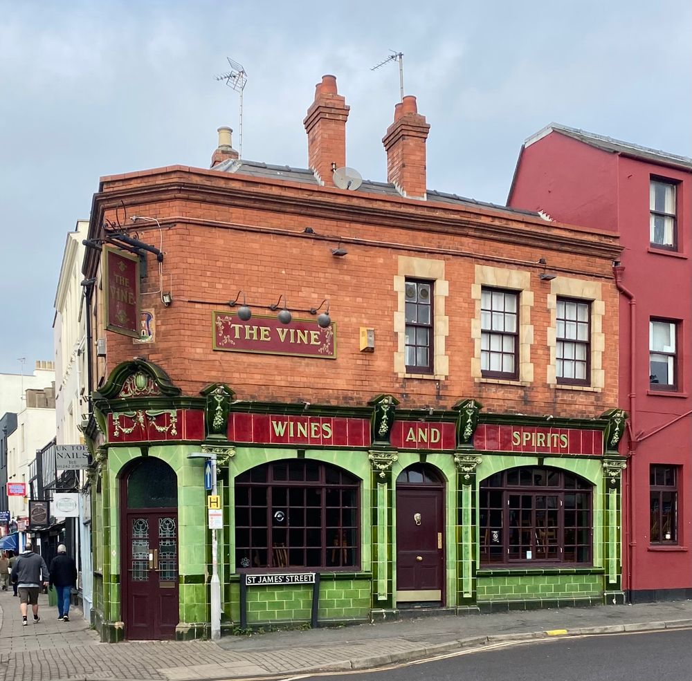 Victorian pub on corner site, the ground floor tiled in green and red (with tiled pilasters and capitals); the upper floor is red brick with stone dressings. 
