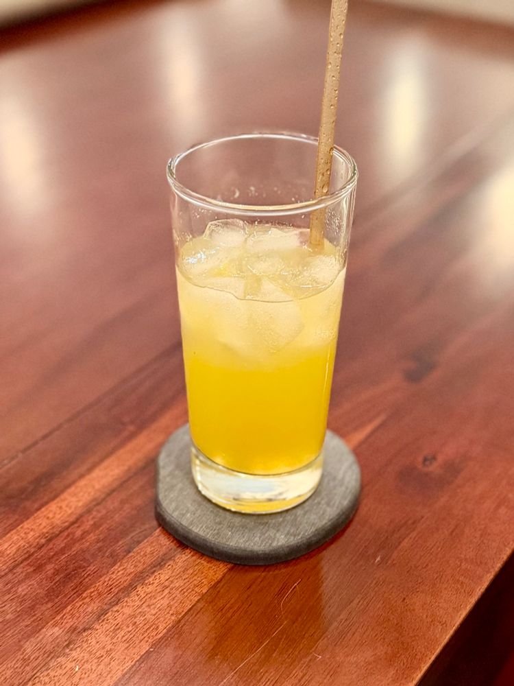 A highball glass mostly full of a yellow liquid and ice. There is a brown straw in the drink.