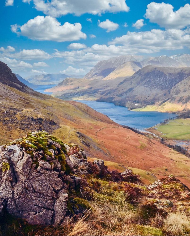 View down to a valley with a crystal clear lake.. soft tones and white fluffy clouds above. 