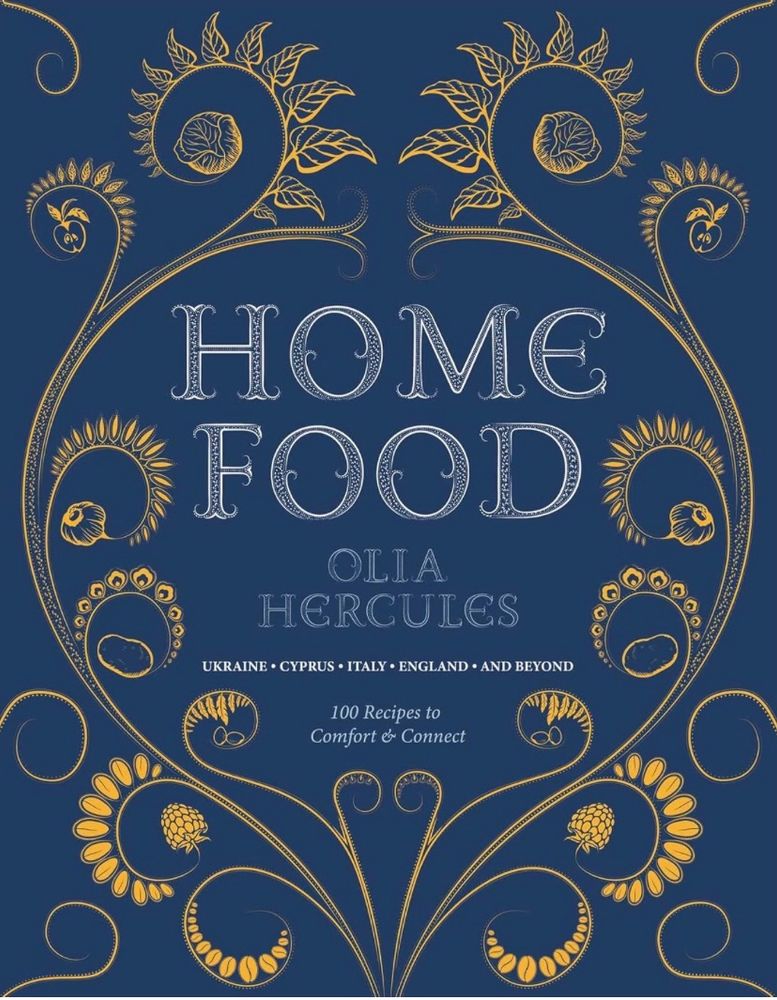 The book cover of Olia Hercules’ HOME FOOD with beautiful hand drawn swirly plants, including cabbages, apples and raspberries, surrounding the title & author’s name in white on a blue background.