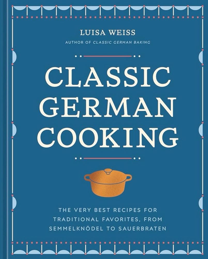 Book cover of Luisa Weiss’ CLASSIC GERMAN COOKING with the title and author’s name in white on a blue background. There is a small taupe coloured baking pot under the title and some light blue scalloped edging around the edges of the book.