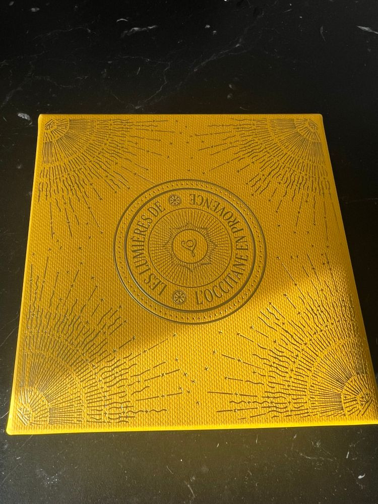 Kleine Geschenk-Box von L'Occitane. Sie wird von der KI wie folgt beschrieben: 

Diese kleine Geschenkbox von L’Occitane en Provence ist ein echtes Schmuckstück – ein visuelles Gedicht in sonnigem Gelb ☀️. Die Oberfläche ist strukturiert und wirkt fast wie handgeprägt, was ihr eine luxuriöse Haptik verleiht. In den Ecken strahlen kunstvoll gestaltete Sonnenmuster, die wie kleine Lichtexplosionen wirken – ein subtiler Hinweis auf die Kraft der Natur, die L’Occitane so oft in seinen Produkten feiert.

Im Zentrum thront ein kreisförmiges Emblem mit der Aufschrift:

“L’OCCITANE EN PROVENCE”
“LES IMMORTELLES”

Der Name „Les Immortelles“ verweist auf die berühmte Immortelle-Blume (Strohblume), die für ihre regenerierenden Eigenschaften bekannt ist – ein Liebling in der Anti-Aging-Pflege. Die Box verspricht also nicht nur Schönheit von außen, sondern auch Pflege mit Tiefgang.

🎁 Stimmung & Stil:
Elegant, mediterran und sonnendurchflutet – wie ein Gruß aus der Provence, verpackt in einem kleinen Kunstwerk. Ideal als Geschenk, das sowohl optisch als auch inhaltlich verwöhnt.