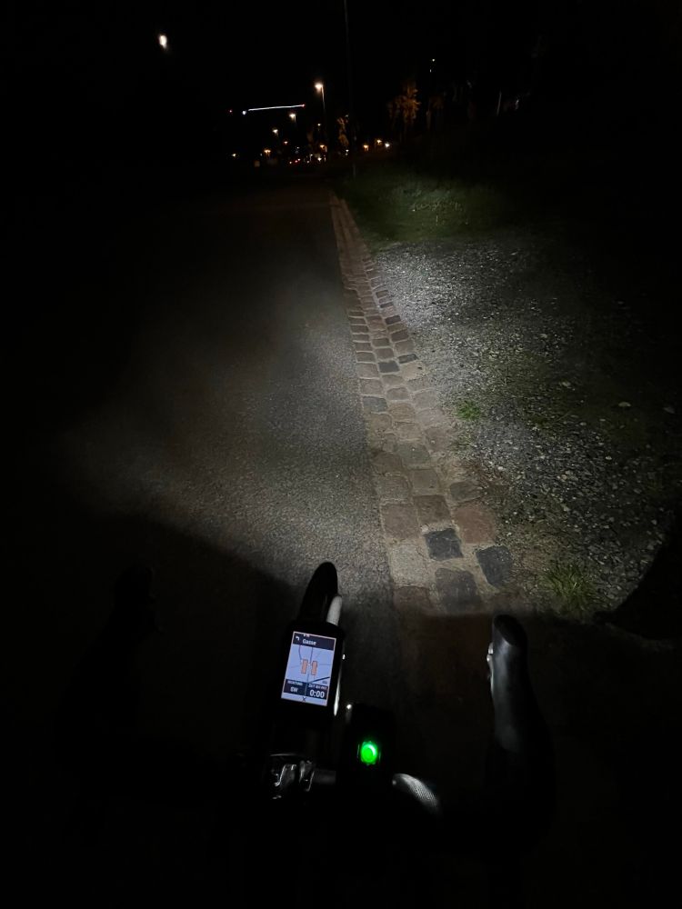 Garmin zeigt eine Karte mit Route, deren Führung gerade pausiert.
Im Hintergrund sieht man Straßenbeleuchtung und beleuchtete Gebäude.