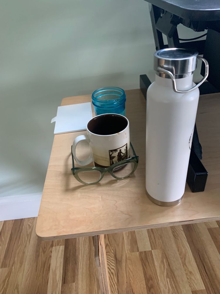 Three beverages sit on a wooden desk next to a pair of glasses. 