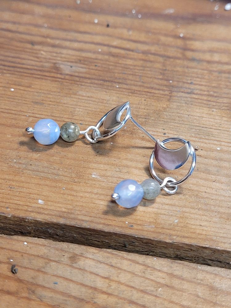 A pair of silver stud earrings. A moon in a circle with dangling beads below it. 