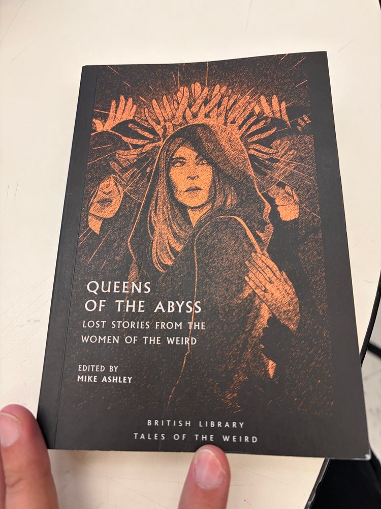 The cover to Queens of the Abyss; Lost Stories From the Women of the Weird. It’s an orange illustration of a hooded occult woman surrounded by shadows of herself, on a black field. 