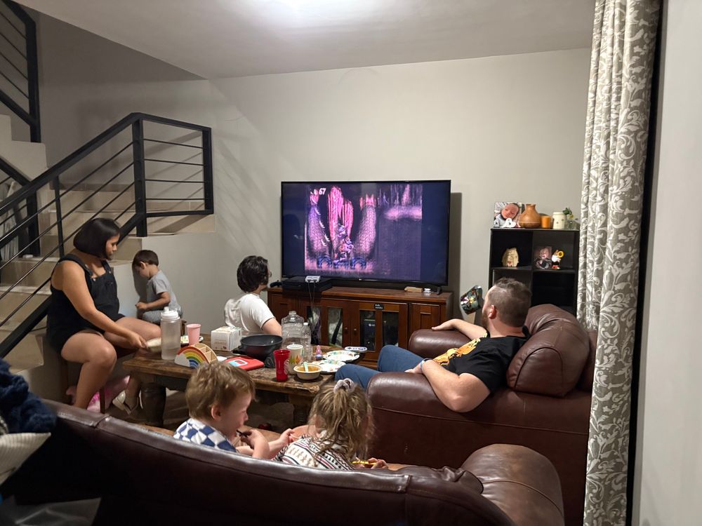A family playing Donkey Kong on an snes game system in the livingroom, eating snacks and having fun