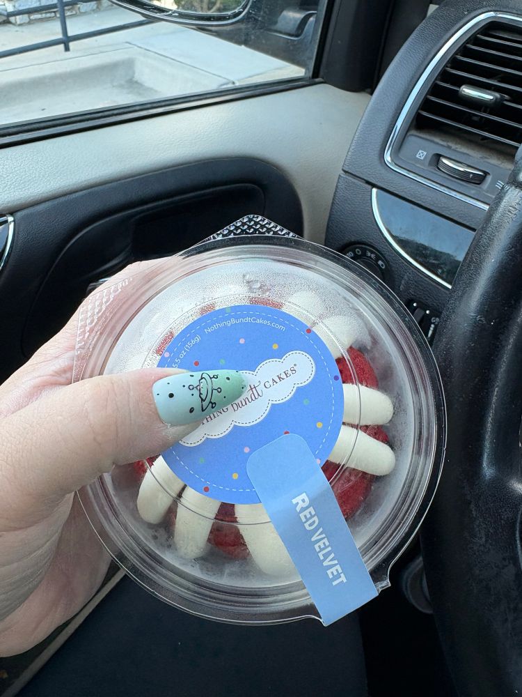 A hand holding a red velvet bundtlet from Nothing Bundt Cakes