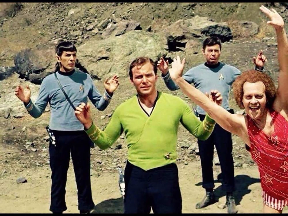 A humorous edited scene from the original Star Trek series. Captain Kirk stands in the foreground with his hands raised, flanked by Spock and Dr. McCoy in the background on a rocky alien landscape. In front, a cheerful Richard Simmons has been digitally added, wearing a bright red workout outfit and waving enthusiastically, contrasting the serious expressions of the crew.