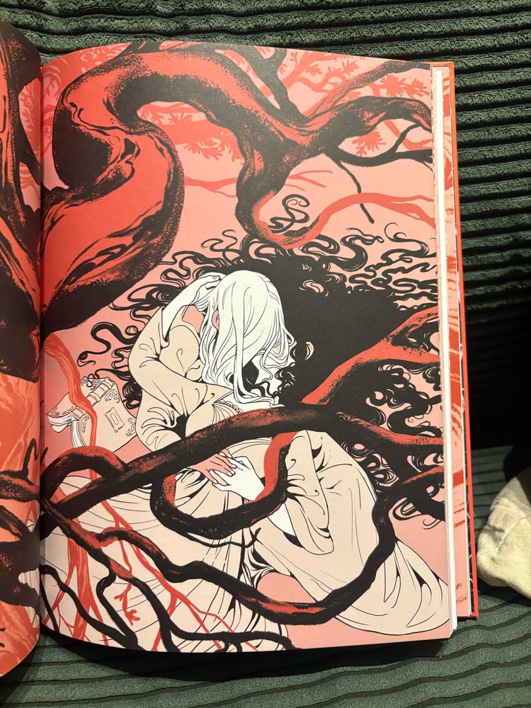 An illustrated page from Beehive Books’ edition of Carmilla. It depicts one woman lying on her back, hair splayed on the ground around her, and another woman leaning over her face to kiss her. Their hands are entwined over the first woman’s waist. A book sits, forgotten, on the ground beside them.