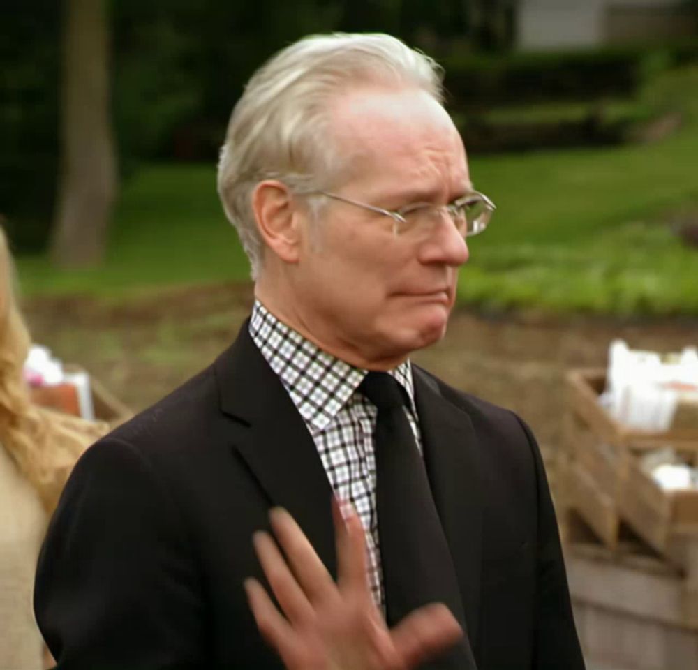 a man wearing glasses and a black suit stands in front of a green field