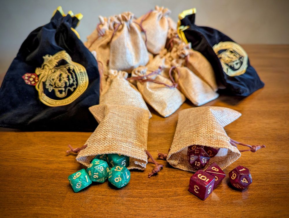 A number of small burlap sacks are piled on a lacquered stained dining table. The two burlap sacks nearest to the camera are open, revealing the dice spilling out.

One set is a marbled green, and the other is opalescent red. Both have gold lettering.

There are also two black velvet bags with gold tiger and dragon sigils printed on them. The dragon curls around the head of the tiger and facing a 20 sided die.