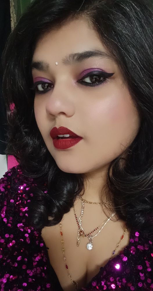 A woman in a purple 🟣 sequin dress, purple eyeshadow, and maroon lipstick 