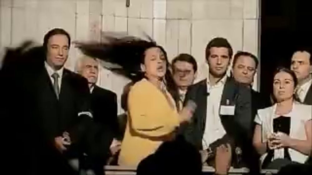 a woman in a yellow jacket is dancing in front of a group of people in suits and ties .