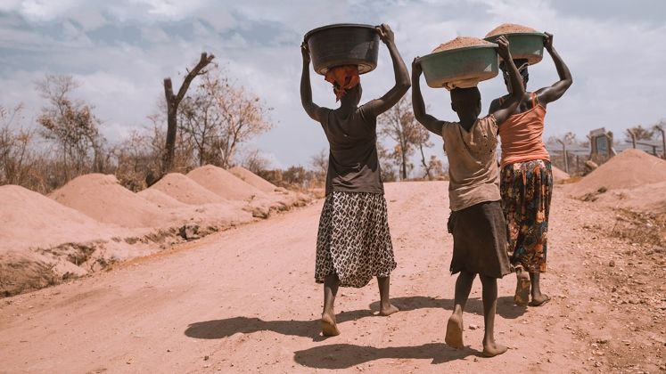 People walking and carrying basins on their heads at Rhino Refugee Camp, Arua, Uganda