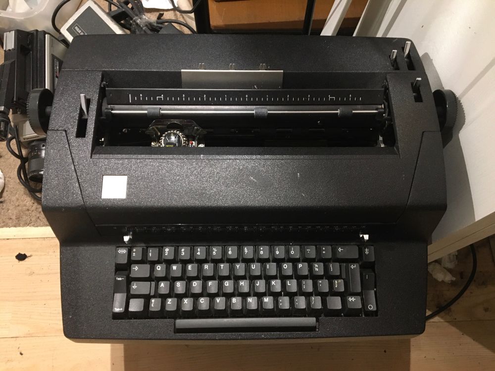 A black electric typewriter sitting on a crate on the floor.