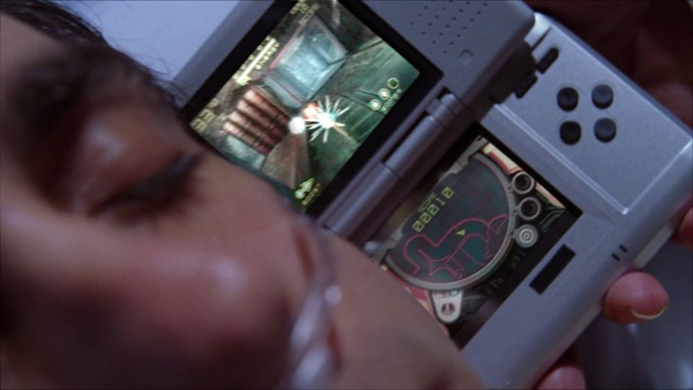 a screenshot of House MD showing Dr. House holding up a Nintendo DS playing the pack-in demo of Metroid Prime Hunters to a comatose patient's ear to check if he's actually in a coma