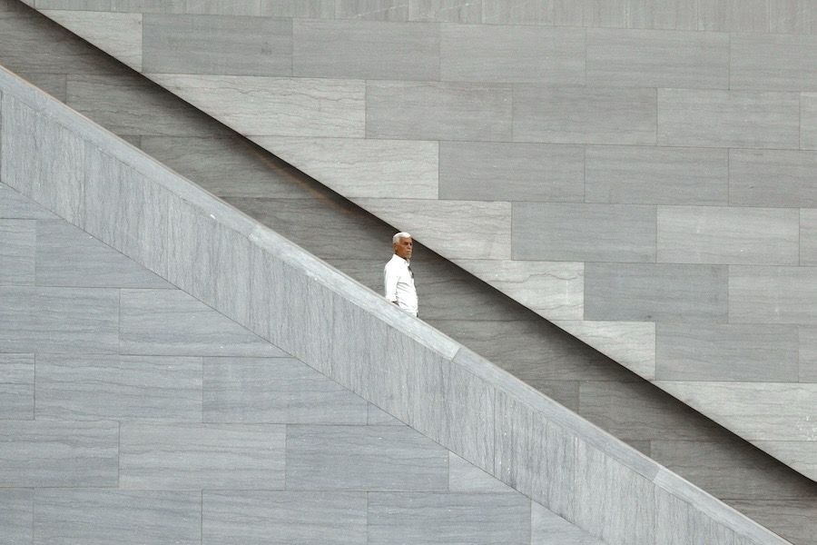 A man descending on a stairway diagonally crossing the image. Above and below stone walls.