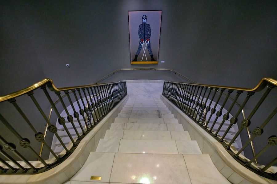 Color image of a stairway seen from above. A painting in the back centre with stairway bifurcated on each side.