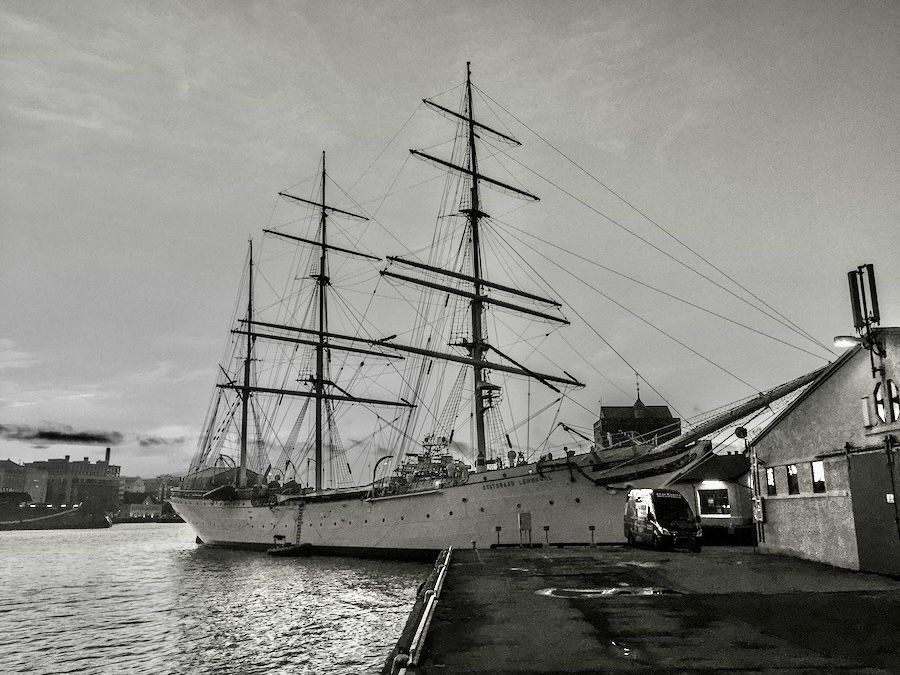 A b/w image of an anchored sailing ship on an evening with clear skies.