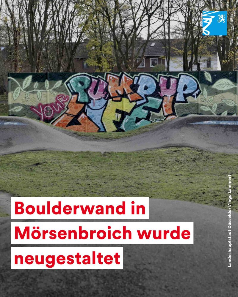 Graffiti mit der Aufschrift 'Pump Up Your Life' an einer neu gestalteten Boulderwand in Mörsenbroich, umgeben von Bäumen und Wohnhäusern.