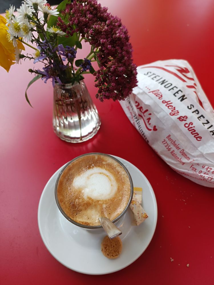 eine tasse flat white und blumen und eine bäckertüte