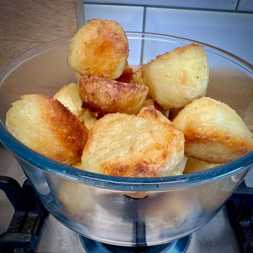 A glass bowl full of golden freshly roasted potatoes 