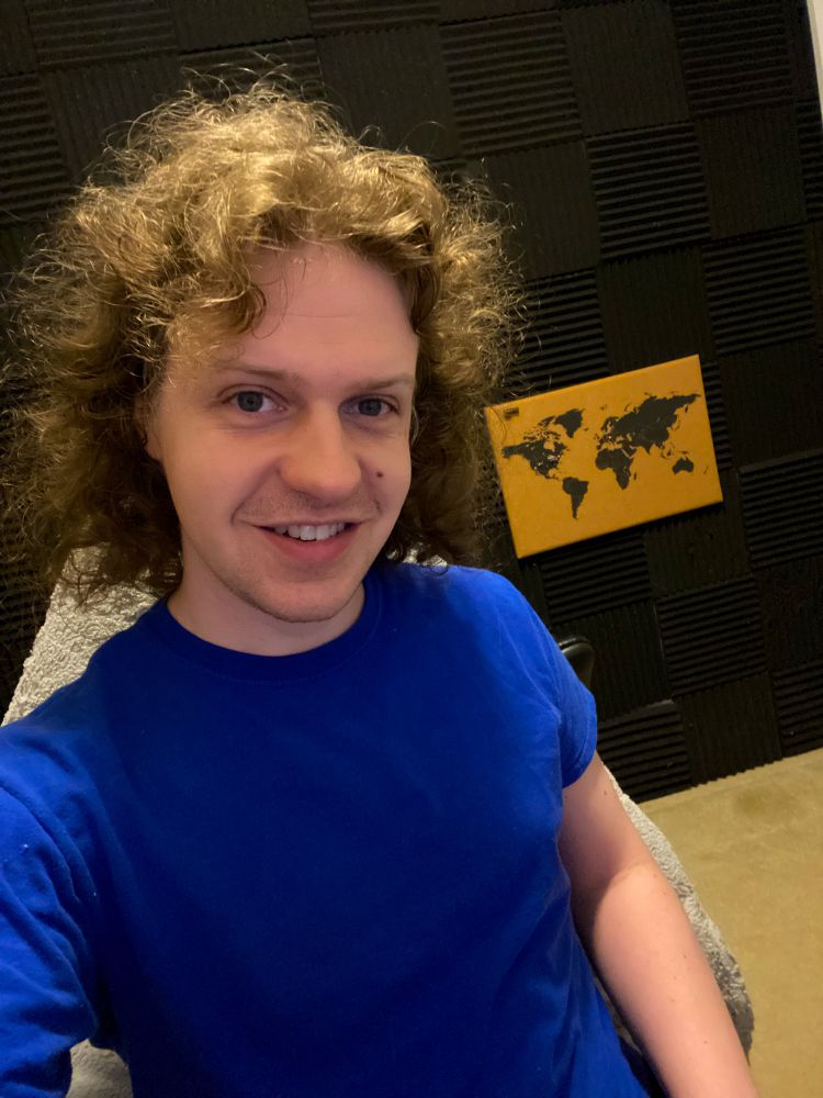 Joycenator sitting in their office, wearing a blue t-shirt and smiling into the camera 