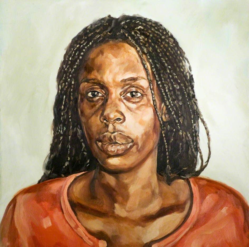 Portrait of Barbara with long braided hair, wearing a loose orange top against a plain light background.