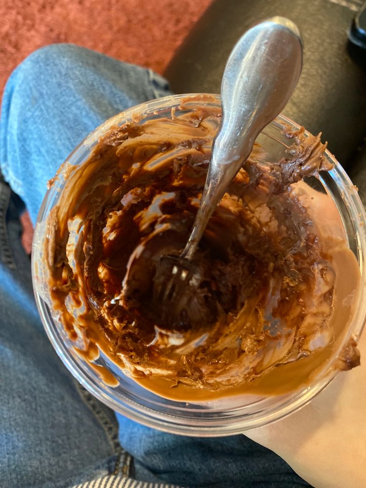 A top view of a clear cup with chocolate covering the inside, a fork sitting in it.