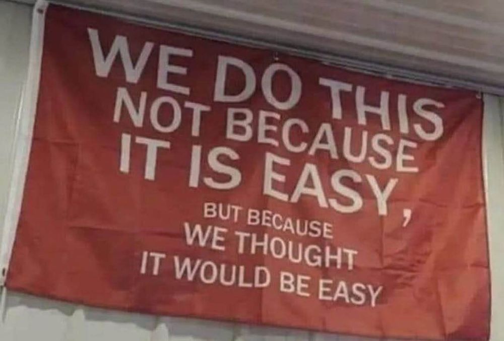 A flag in a wall that reads "We do this not because it is easy, but because we thought it would be easy"