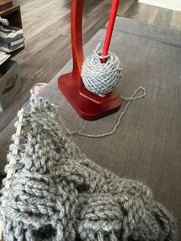 Grey yarn on a yarn stand linked to a project on circular knitting needles 
