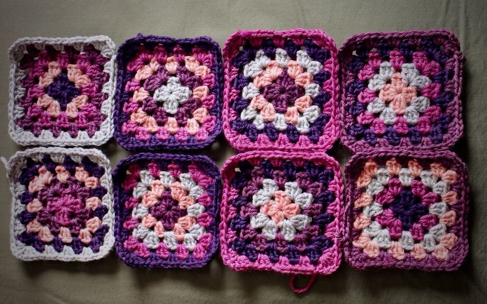 Eight crocheted granny squares made up of various shades of purple and pink on a grey background
