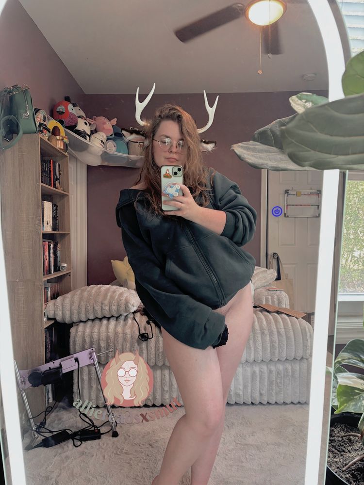 allie standing in front of a mirror. she's wearing an oversized dark green hoodie. atop her head is a set of brown speckled deer ears & white antlers. 