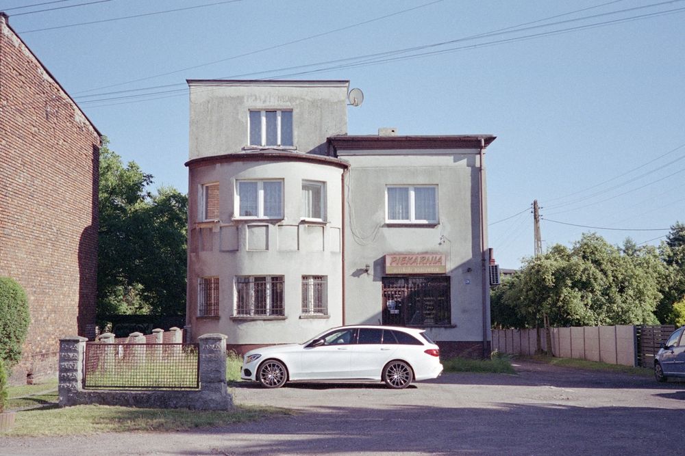 a house / bakery with a faded sign with a white car parked directly in front