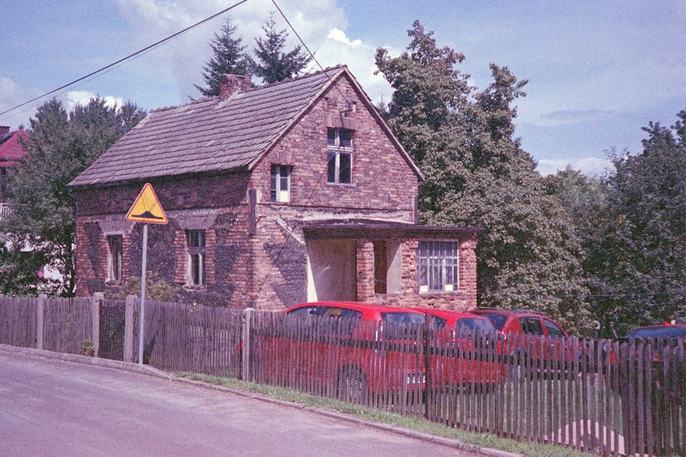 a tiny brick house with multiple red cars next to it, behind a wooden fence