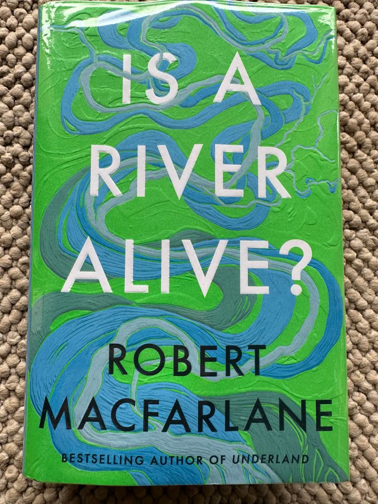 Photo of a book called ‘Is a River Alive’ by Robert Macfarlane. Stylised swirly blue river on a green background. 