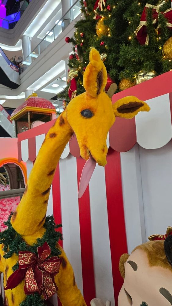 Foto de uma girafa xoxa capenga com a lingua de fora. É uma decoraçao de natal de shopping