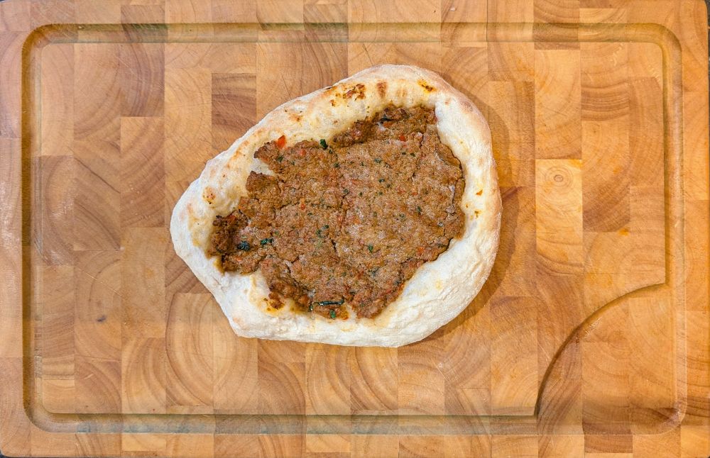 Photo of my attempt at Lahmajun, an Armenian flatbread topped with a spiced lamb mixture. It looks a bit like a pizza with a very meaty sauce. 