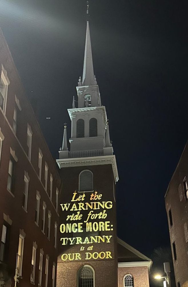 Photo from April 18, 2025 of the Old North Boston Church with lit words projected on the side: "Let the warning ride forth once more: Tyranny is at our door."